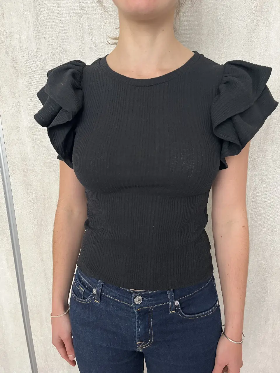 Blusa negra de tejido de punto con mangas con volados. Ideal para un look elegante y moderno.