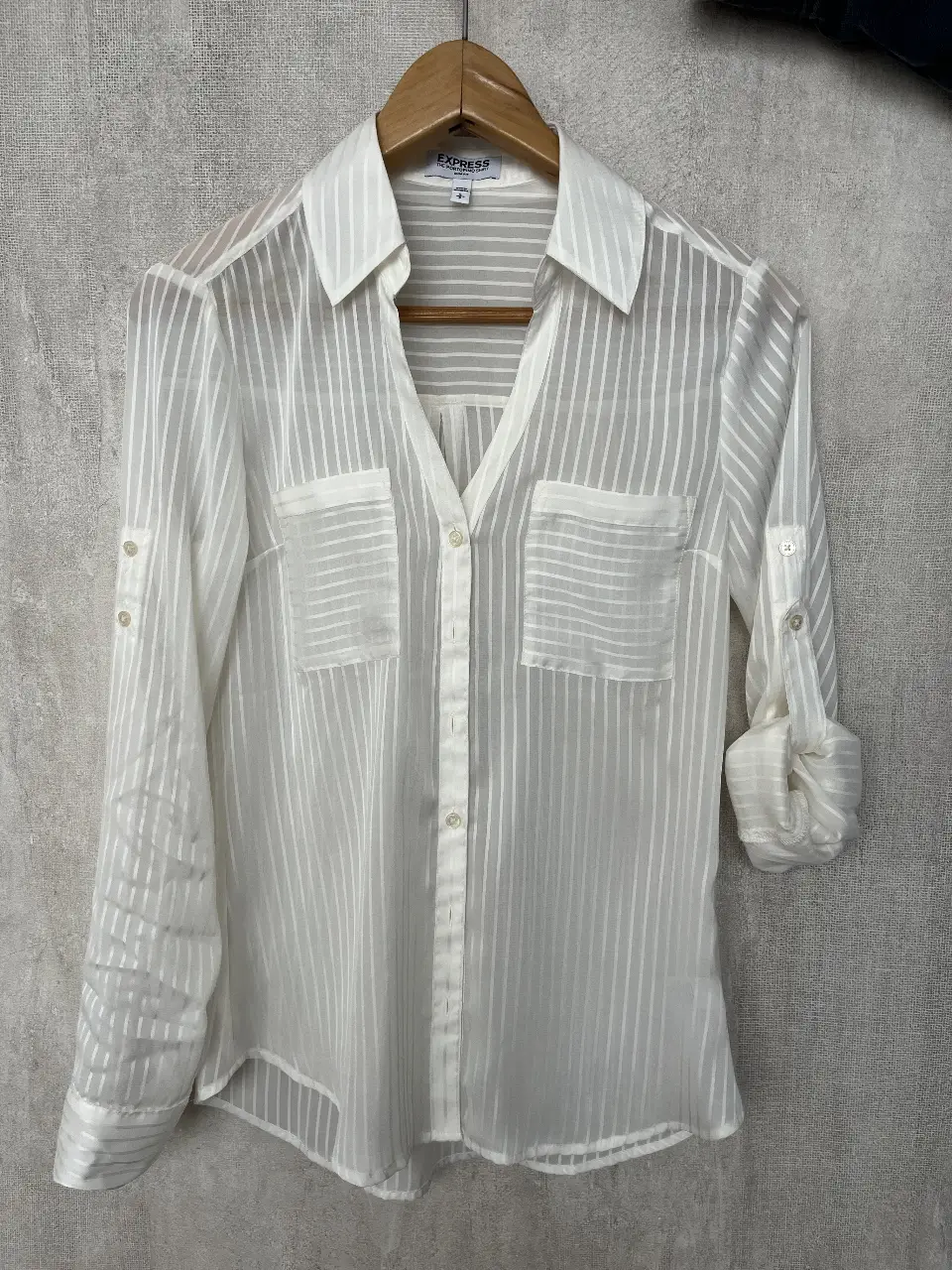 Camisa blanca de la marca Express, modelo Portofino, con rayas verticales. Tiene mangas largas con botones para ajustar y bolsillos en el pecho. Ideal para un look casual o de trabajo.