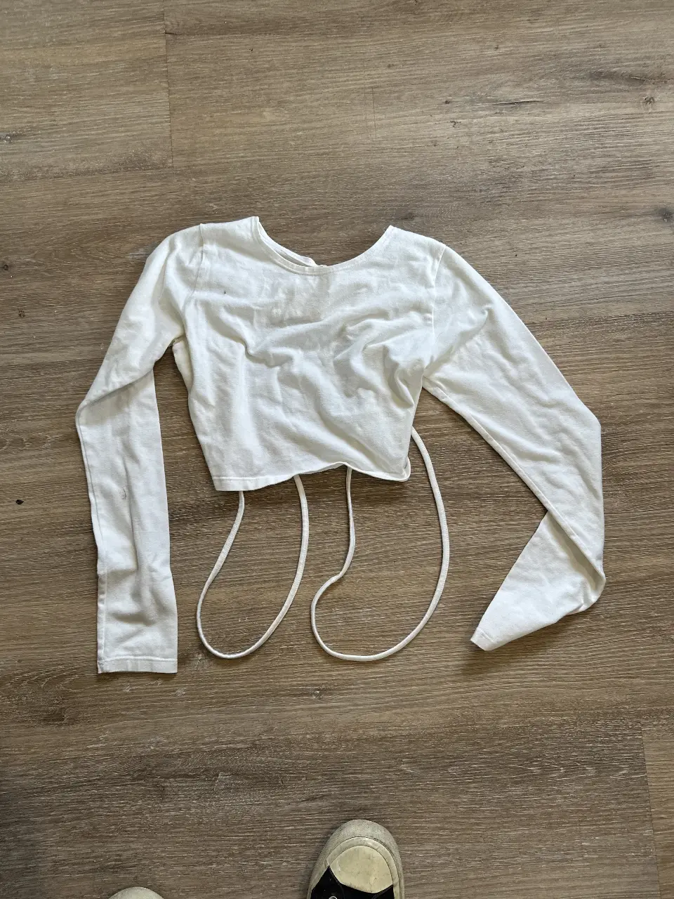 Crop top blanco de manga larga con espalda descubierta y lazos ajustables. Ideal para un look moderno y versátil.
