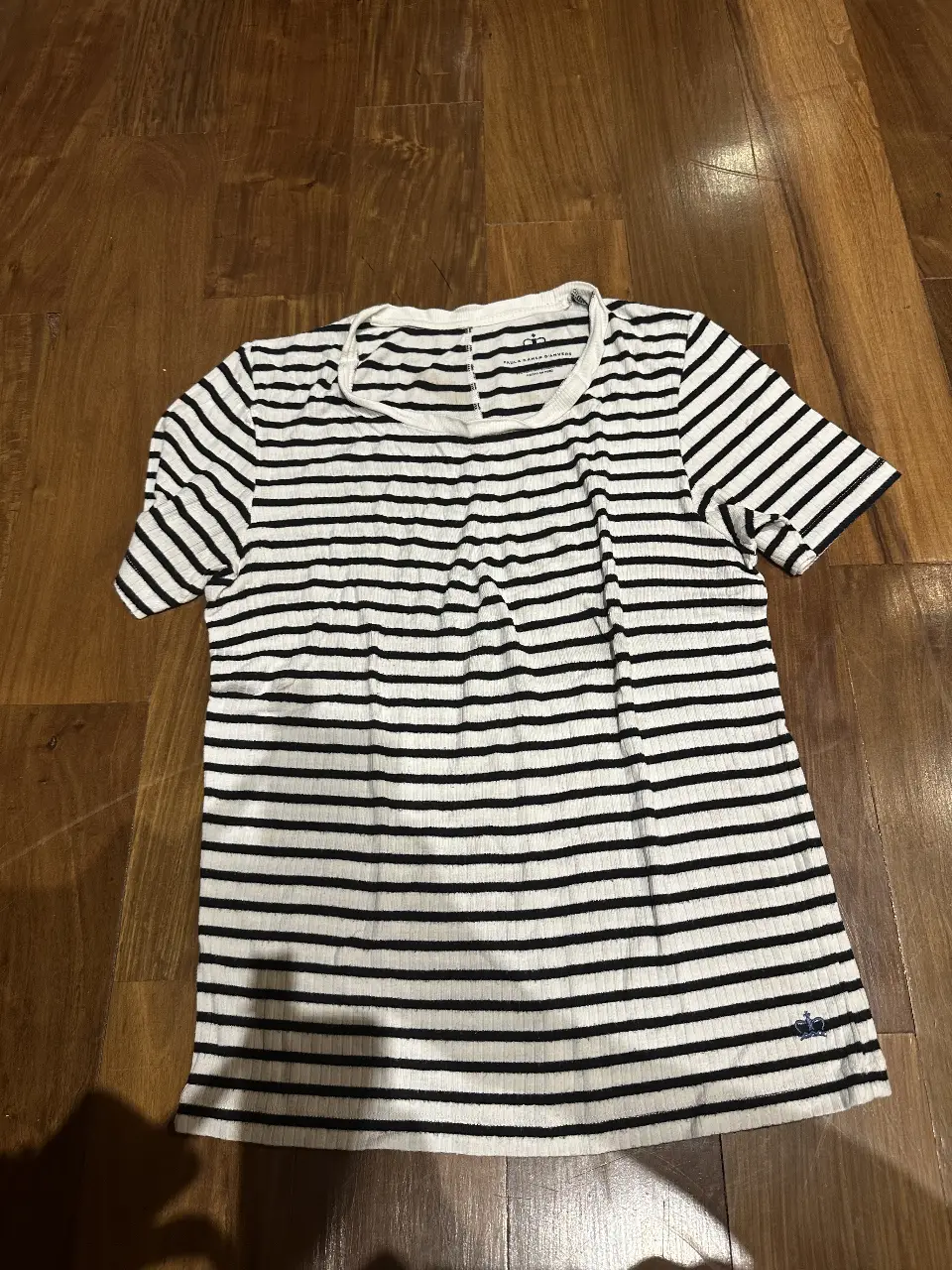 Remera a rayas horizontales en blanco y negro, de manga corta y cuello redondo. Confeccionada en tejido de punto con un pequeño logo bordado en la parte inferior. Ideal para un look casual y versátil.