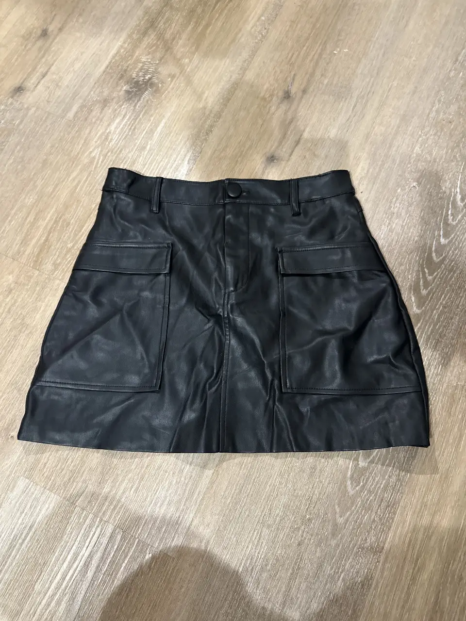 Minifalda de cuero sintético negra con bolsillos delanteros. Tiene hecho un arreglo para que vaya mejor a la cintura
