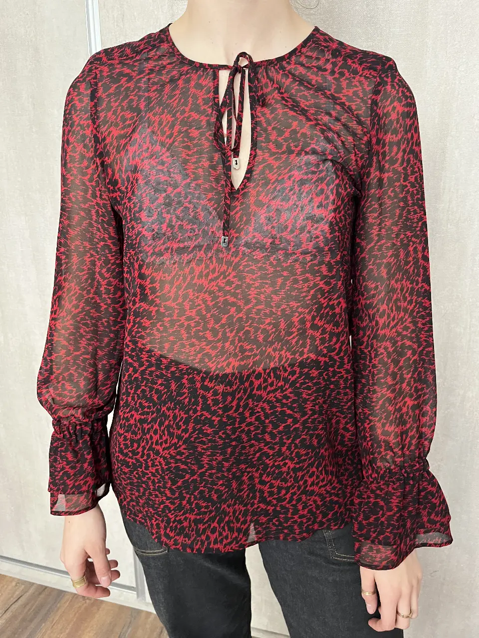 Blusa de mujer con estampado de leopardo en rojo y negro, de tela transparente. Tiene mangas largas con puños y un detalle de lazo en el cuello. Ideal para un look elegante y audaz.
