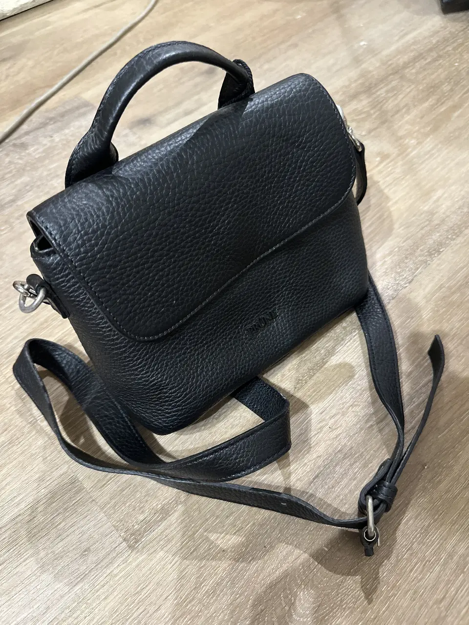 Cartera bandolera negra de cuero con solapa y manija superior. Ideal para llevar lo esencial con estilo y elegancia.