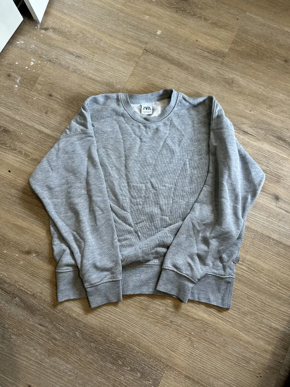 Buzo de cuello redondo de la marca Zara, color gris. Ideal para un look casual y cómodo.