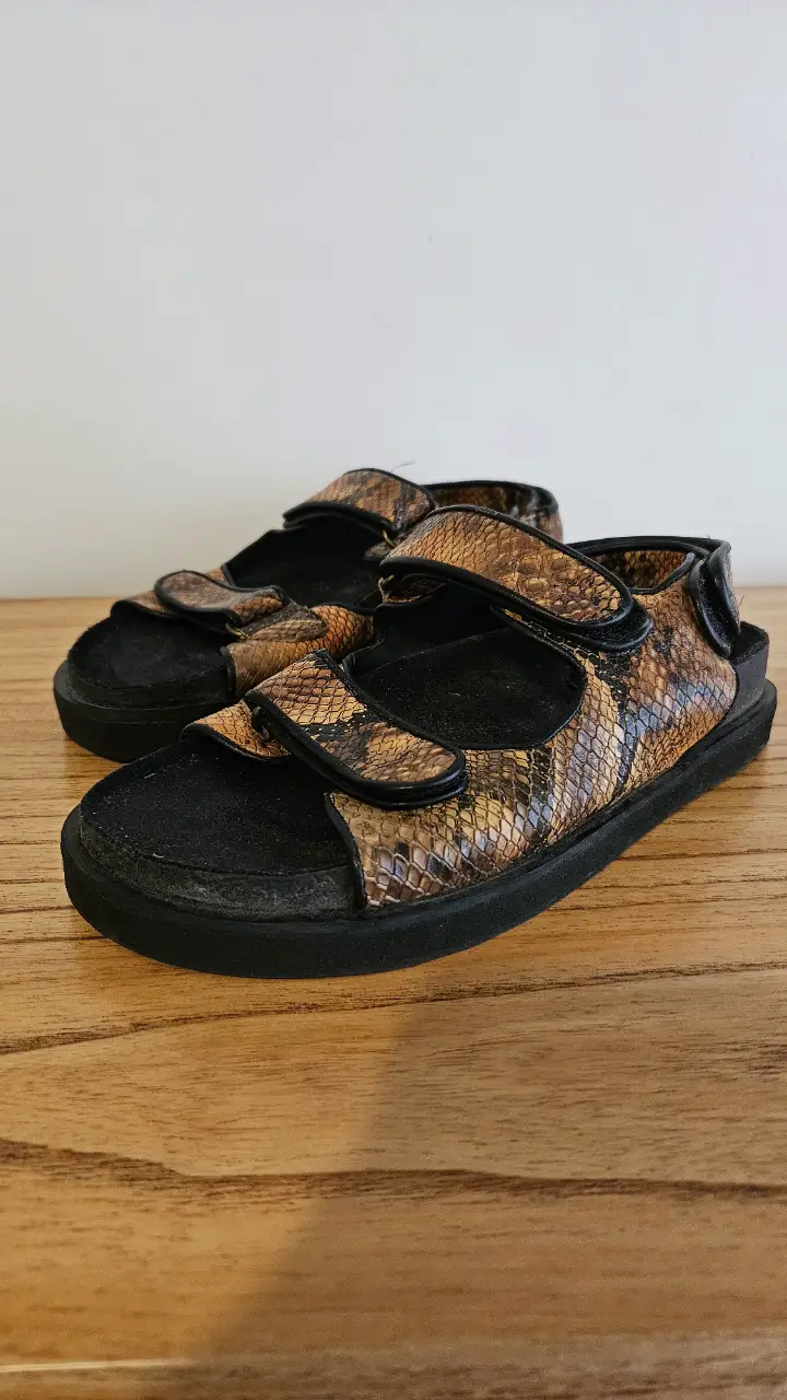 Sandalias de mujer con estampado de piel de serpiente en tonos marrones, con ajuste de velcro y suela negra.