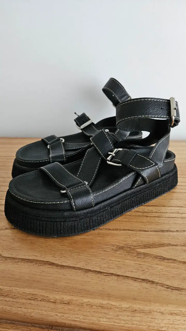 Sandalias negras con plataforma y detalles de costura color claro. Diseño con múltiples tiras y hebillas metálicas para un ajuste seguro y un estilo moderno.