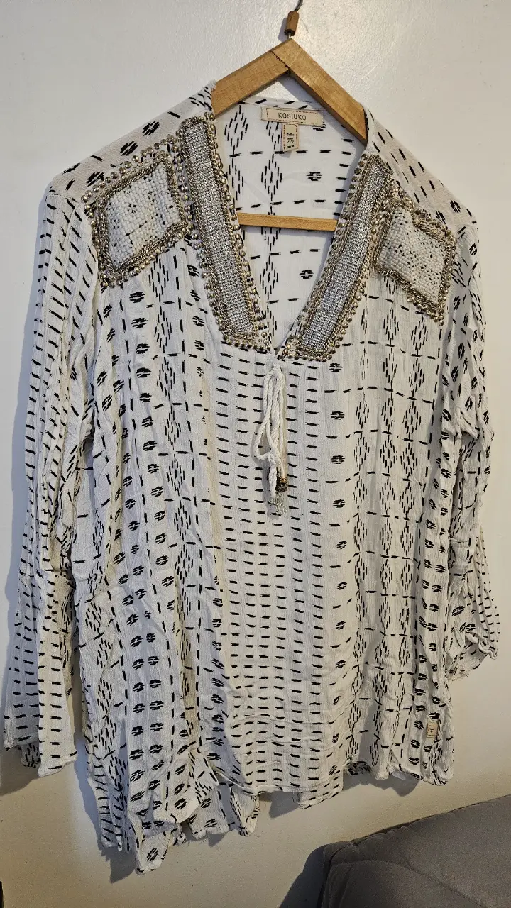 Blusa de mujer mangas largas estilo boho con estampado geométrico en blanco y negro. Detalles bordados y apliques dorados y plateados en el cuello en V. La tela es liviana y fresca, y es talle 42.