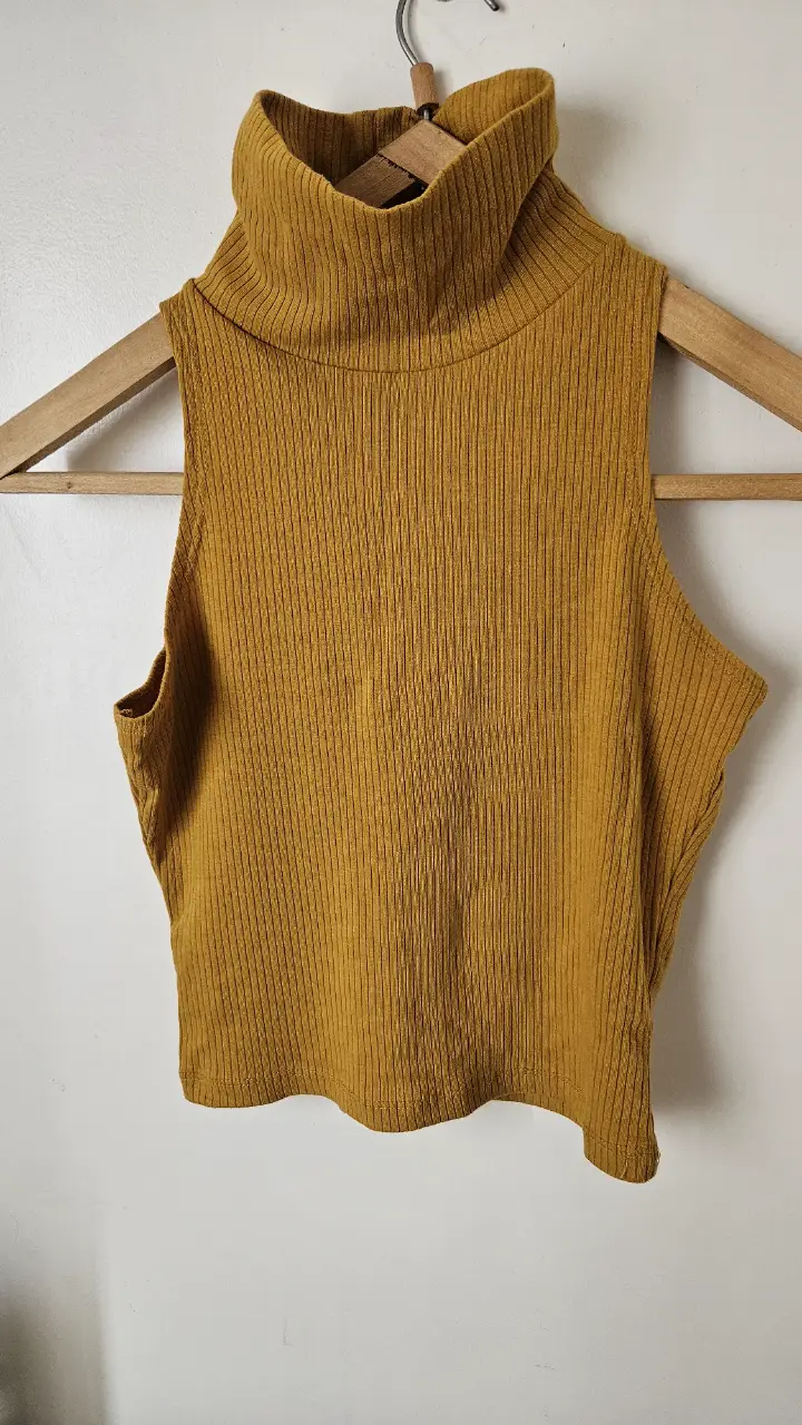 Top tejido de cuello alto sin mangas, color mostaza, ideal para un look moderno y versátil. Perfecto para combinar con jeans o pantalones de vestir.