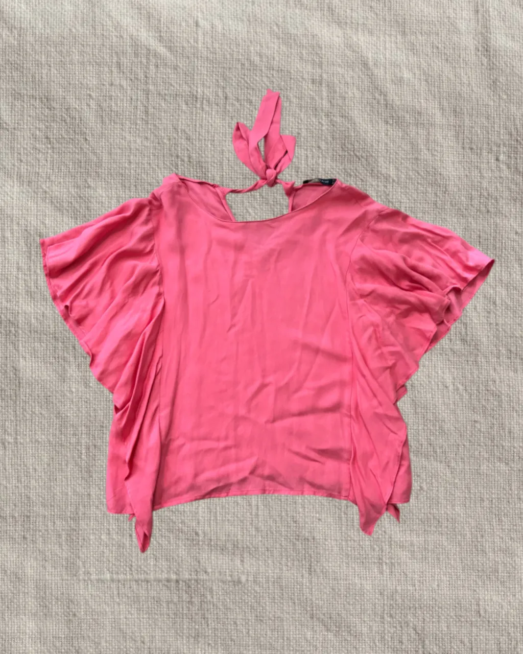 Blusa rosa con mangas amplias con volados y atada en la espalda con un lazo.
