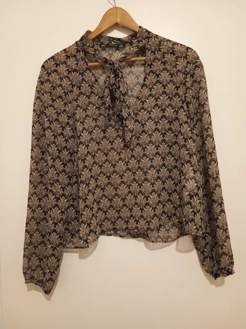 Blusa de mujer de la marca Zara Trafaluc, con estampado floral en tonos negro y crudo. Tiene mangas largas y un lazo en el cuello. Ideal para un look elegante y sofisticado.