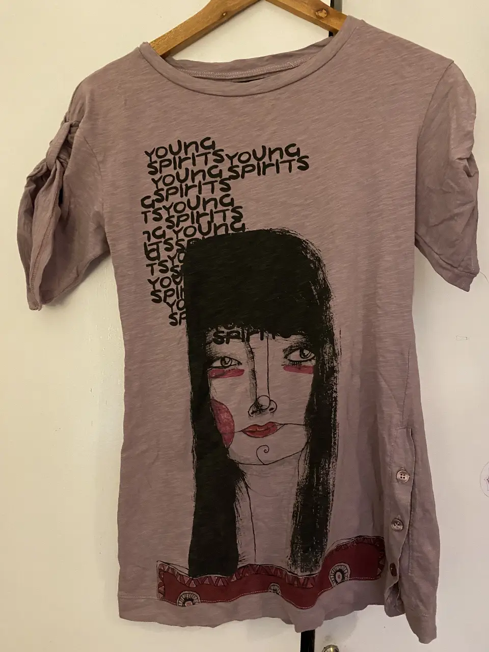 Remera de algodón orgánico Zara, color lila con diseño de rostro y texto. Detalles de mangas con frunces y botones laterales. Talle S.