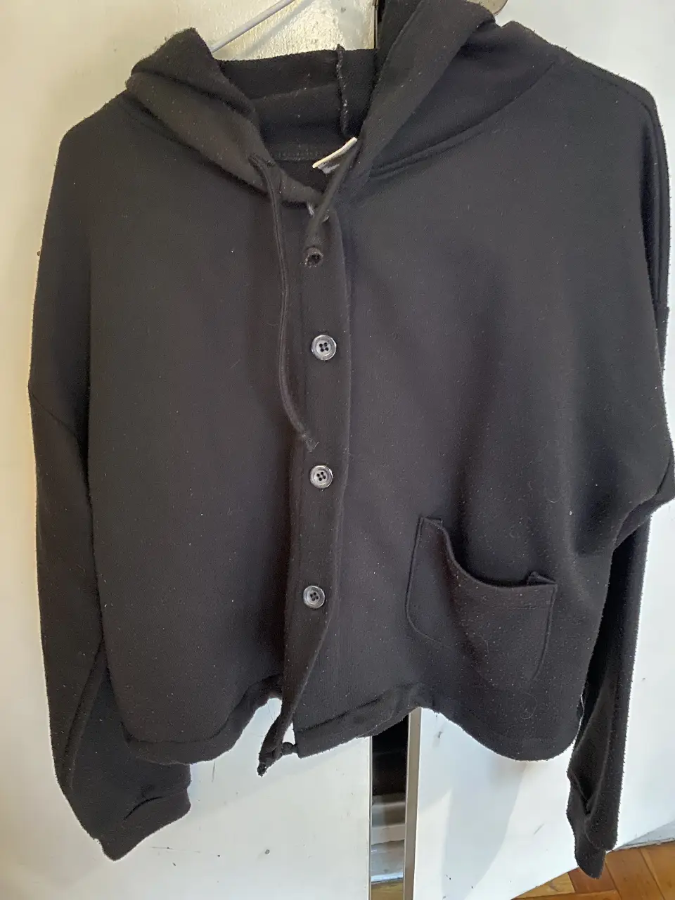 Buzo negro con capucha y botones, ideal para un look casual y cómodo. Con un bolsillo frontal y un diseño versátil, perfecto para el día a día.