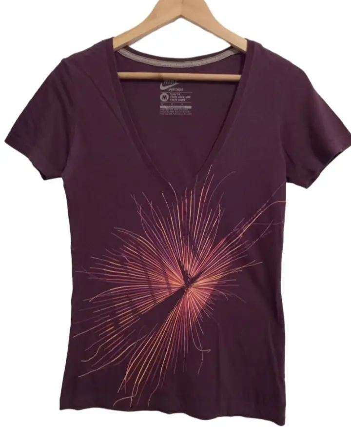Remera Nike de mujer, color violeta con diseño floral en el frente. Cuello en V y manga corta. Ideal para un look casual y deportivo.