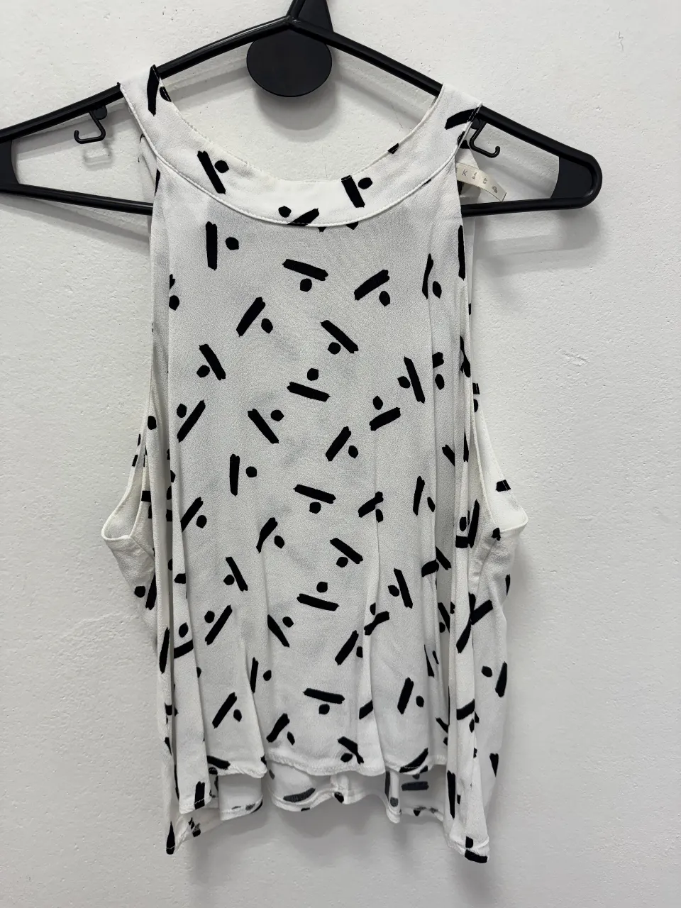 Top blanco con estampado de figuras geométricas negras. Cuello redondo y diseño sin mangas. Ideal para un look casual y fresco.