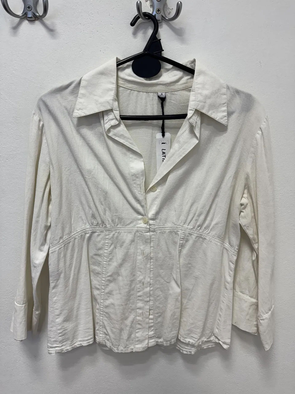 Camisa blanca de mujer, con cuello y mangas largas. Diseño entallado con detalles de costura y un botón en el centro. Ideal para un look casual y elegante.