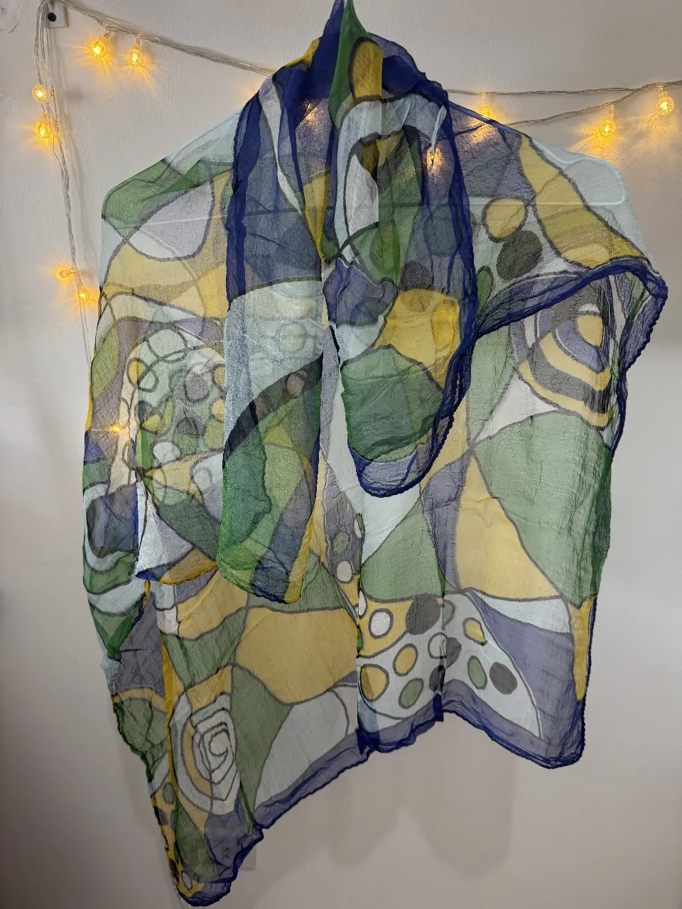 Pañuelo de seda con estampado abstracto en tonos verdes, amarillos y azules. Ideal para complementar cualquier look con un toque de color y estilo.