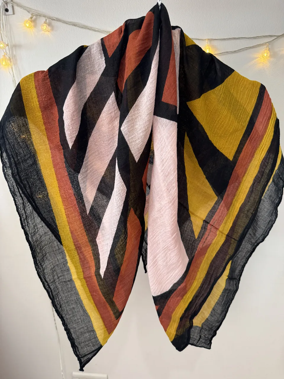 Pañuelo de tela con diseño geométrico en tonos negro, amarillo, naranja y rosa. Ideal para complementar cualquier look.