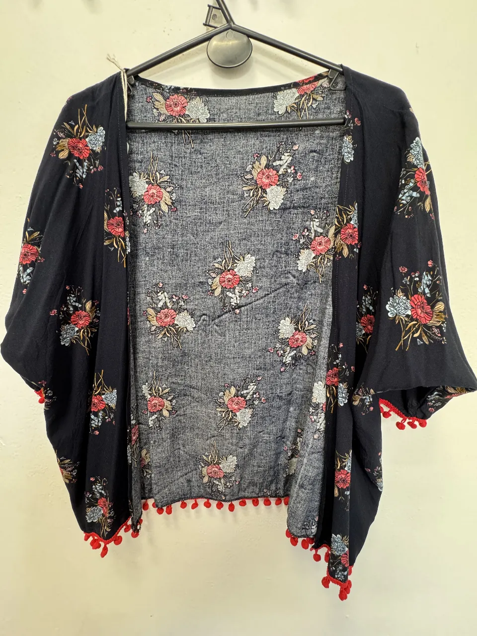 Kimono de mujer con estampado floral en tonos rojos y blancos sobre fondo negro. Detalles de pompones rojos en el borde. Ideal para un look bohemio y casual.