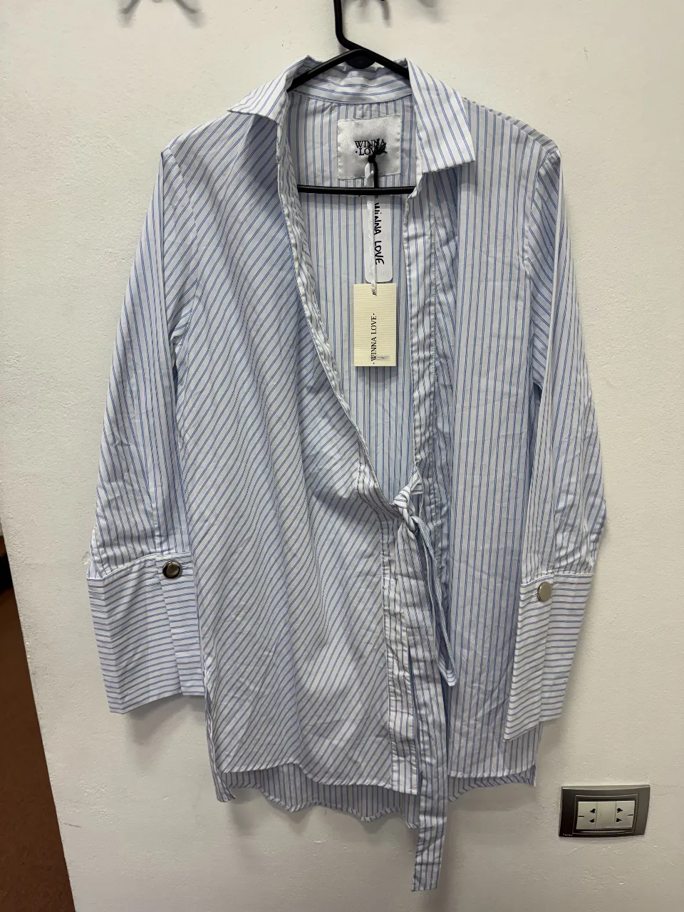 Camisa a rayas celeste y blanca de la marca WINNA LOVE, con cuello camisero y detalle de lazo en la cintura. Posee puños con botones.