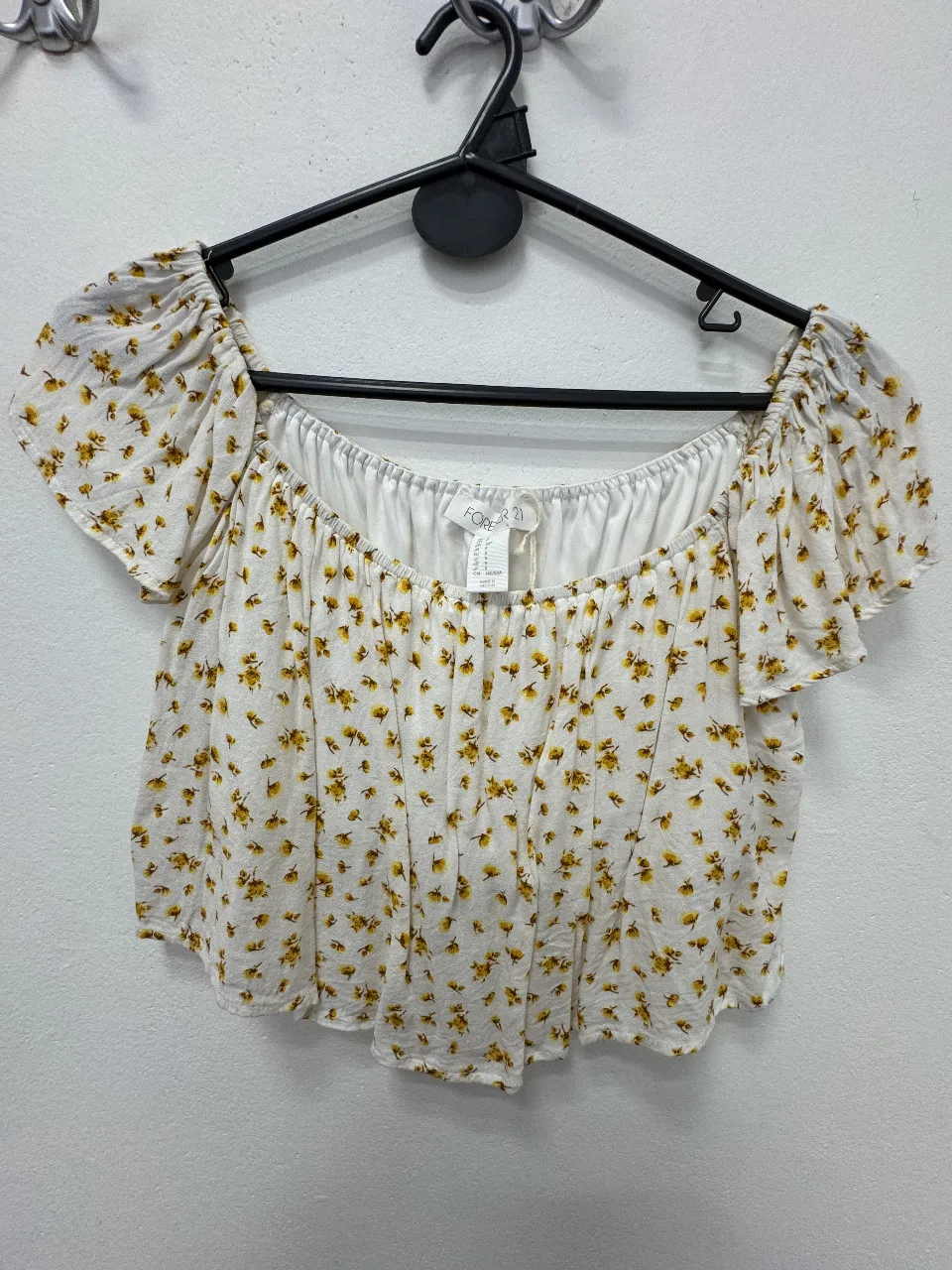 Blusa de mujer con estampado floral en tonos amarillos sobre fondo blanco. Corte off-shoulder con mangas cortas tipo volado. Ideal para un look fresco y primaveral.