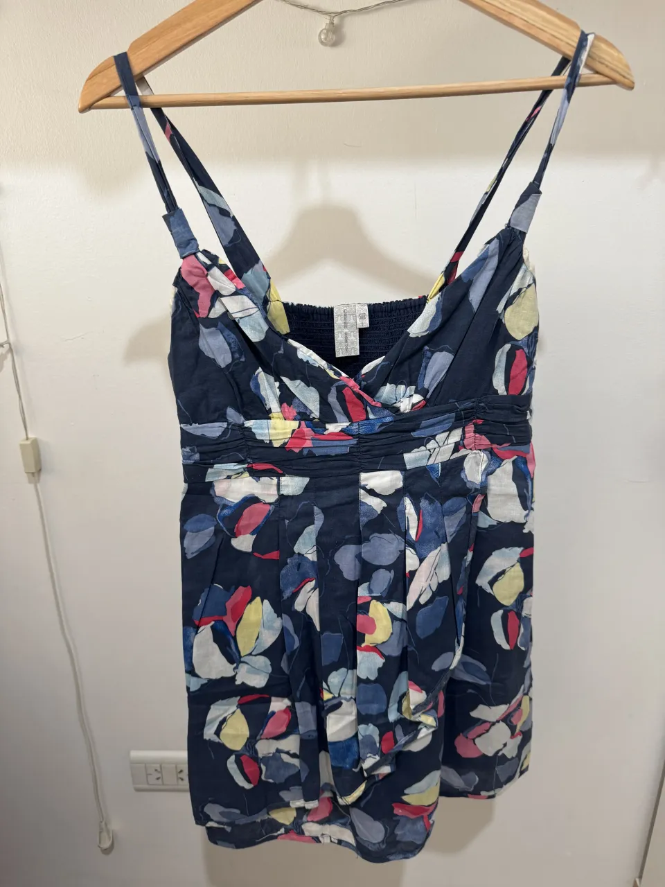 Vestido corto azul oscuro con estampado floral multicolor. Breteles finos y escote cruzado. Cintura con elástico fruncido y falda con pliegues.