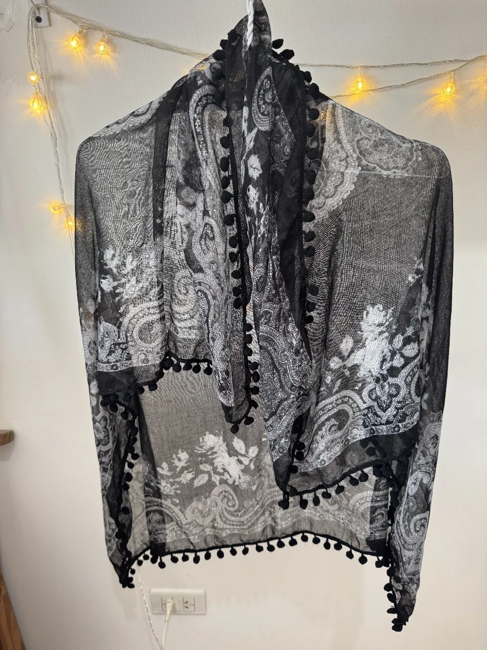 Pañuelo de gasa con estampado floral en blanco y negro, con detalles de pompones en los bordes. Ideal para complementar cualquier look.