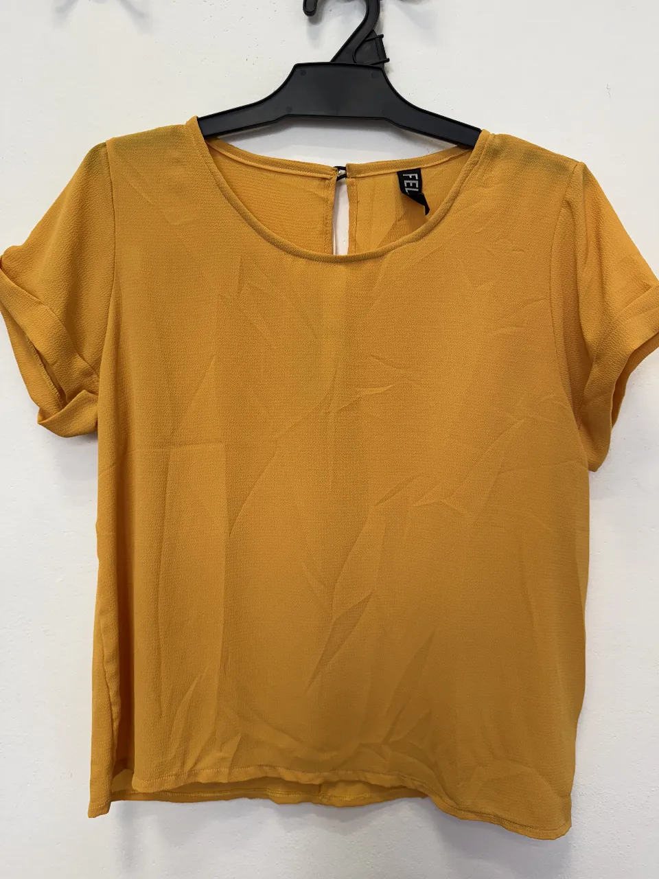 Blusa de mujer color mostaza, con cuello redondo y detalle de abertura en la espalda. Manga corta con dobladillo. Ideal para un look casual y fresco.