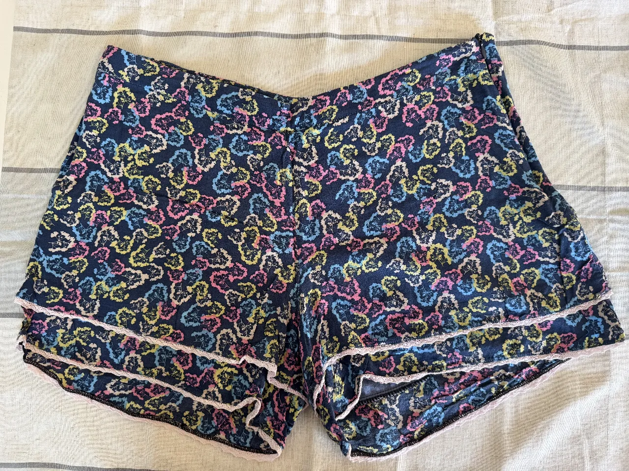 Short de mujer con estampado floral en tonos azules, rosas y amarillos. Detalles de encaje en el borde inferior. Ideal para un look casual y fresco.