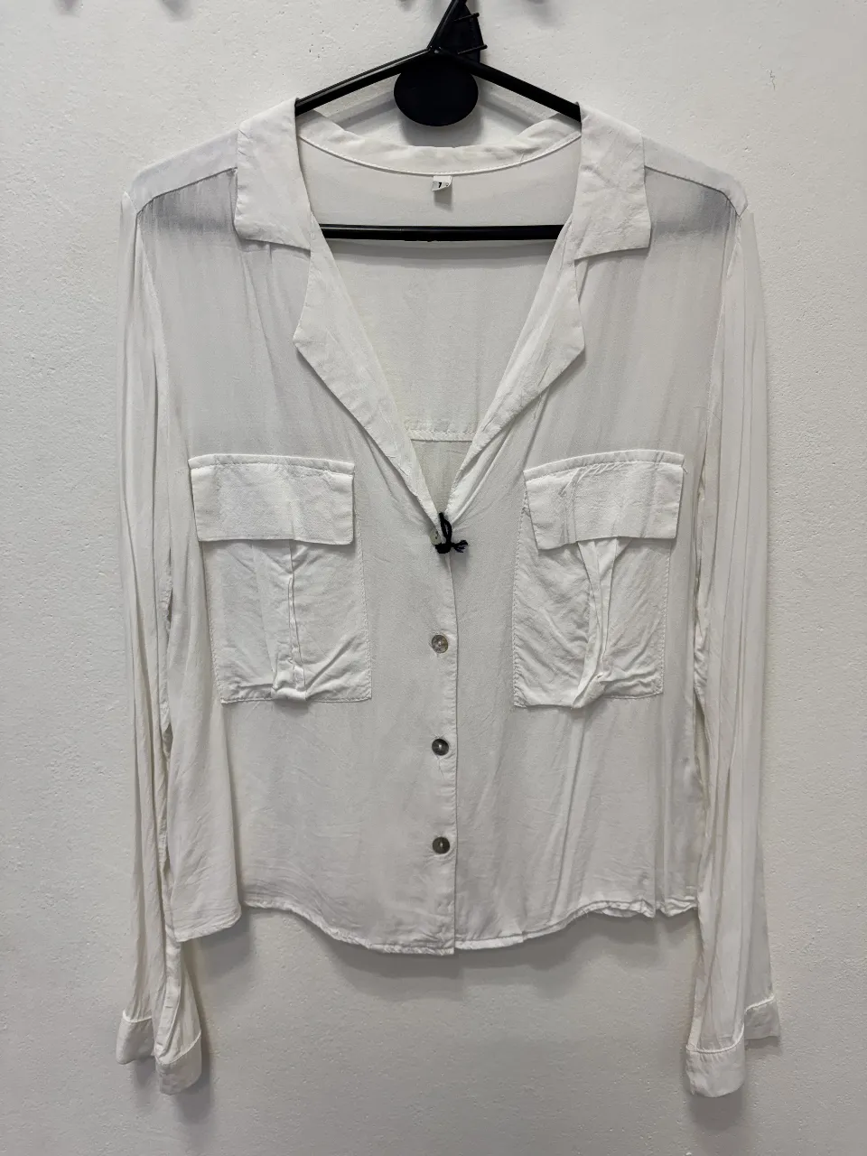Camisa blanca de mujer, con mangas largas y dos bolsillos delanteros. Ideal para un look casual y versátil.