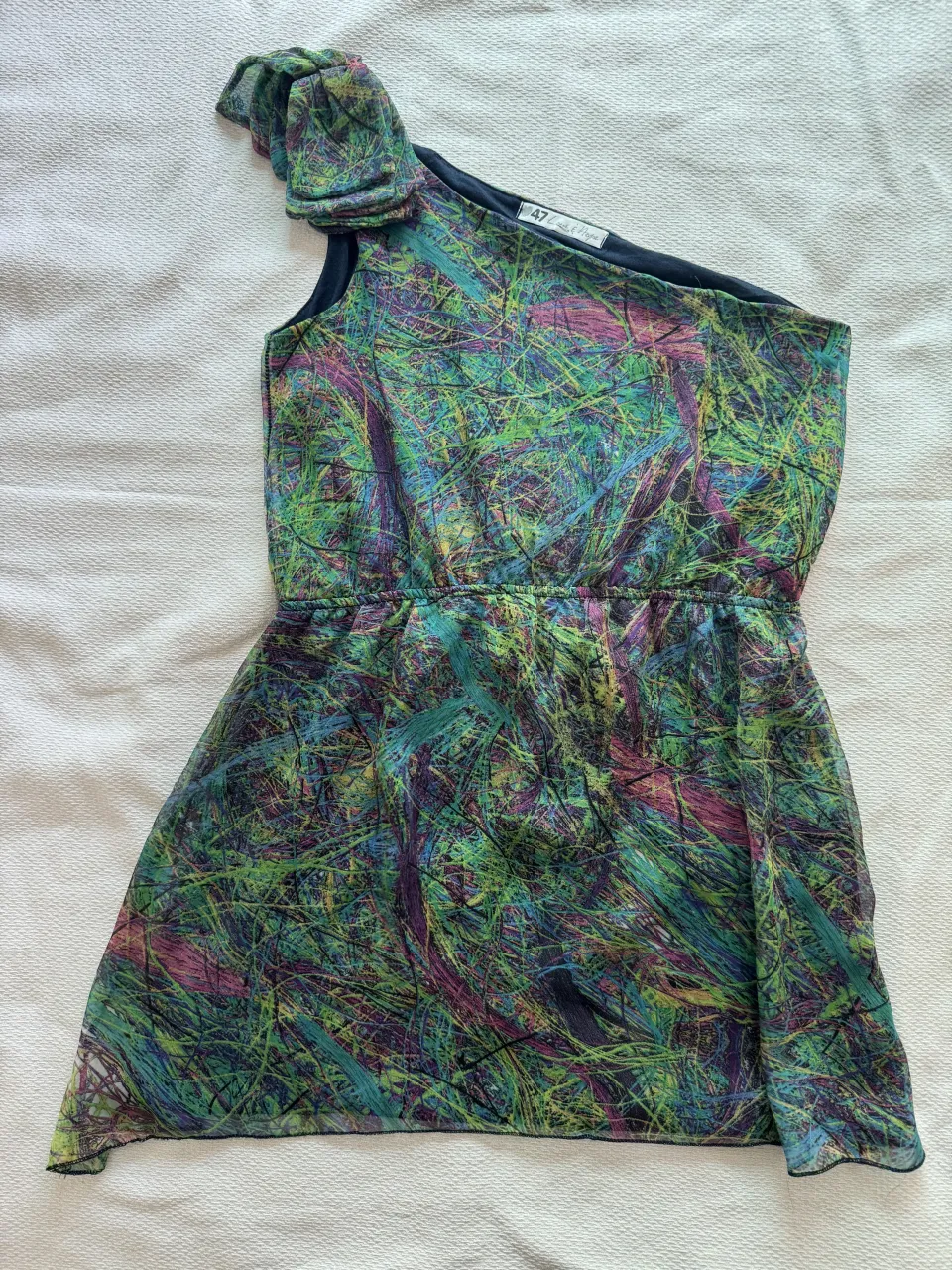 Vestido corto asimétrico con estampa abstracta multicolor. Tiene un solo hombro con detalle de volados y cintura elastizada.