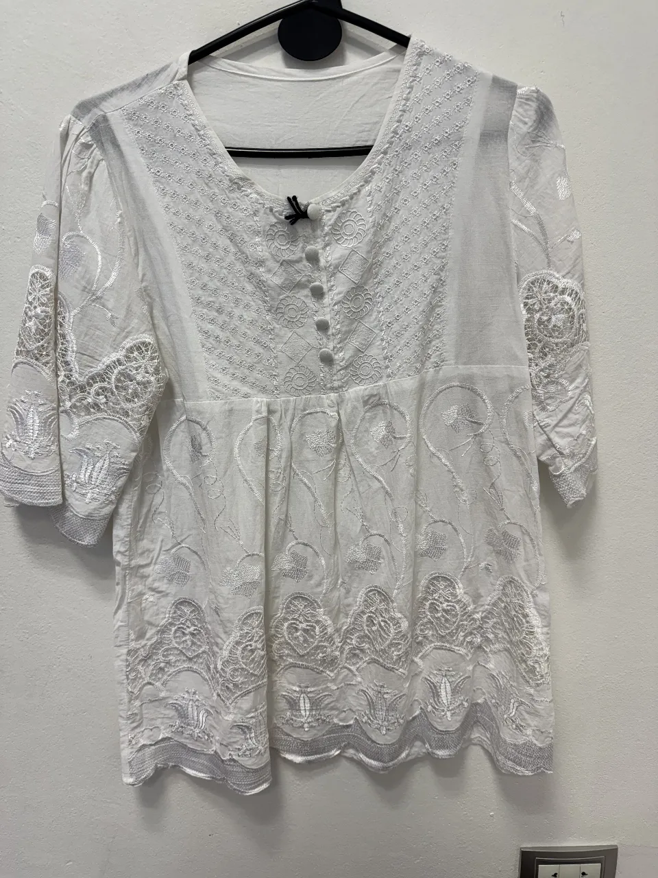 Blusa blanca con bordados y detalles calados. Diseño con mangas 3/4 y botones en la parte delantera. Ideal para un look fresco y femenino.
