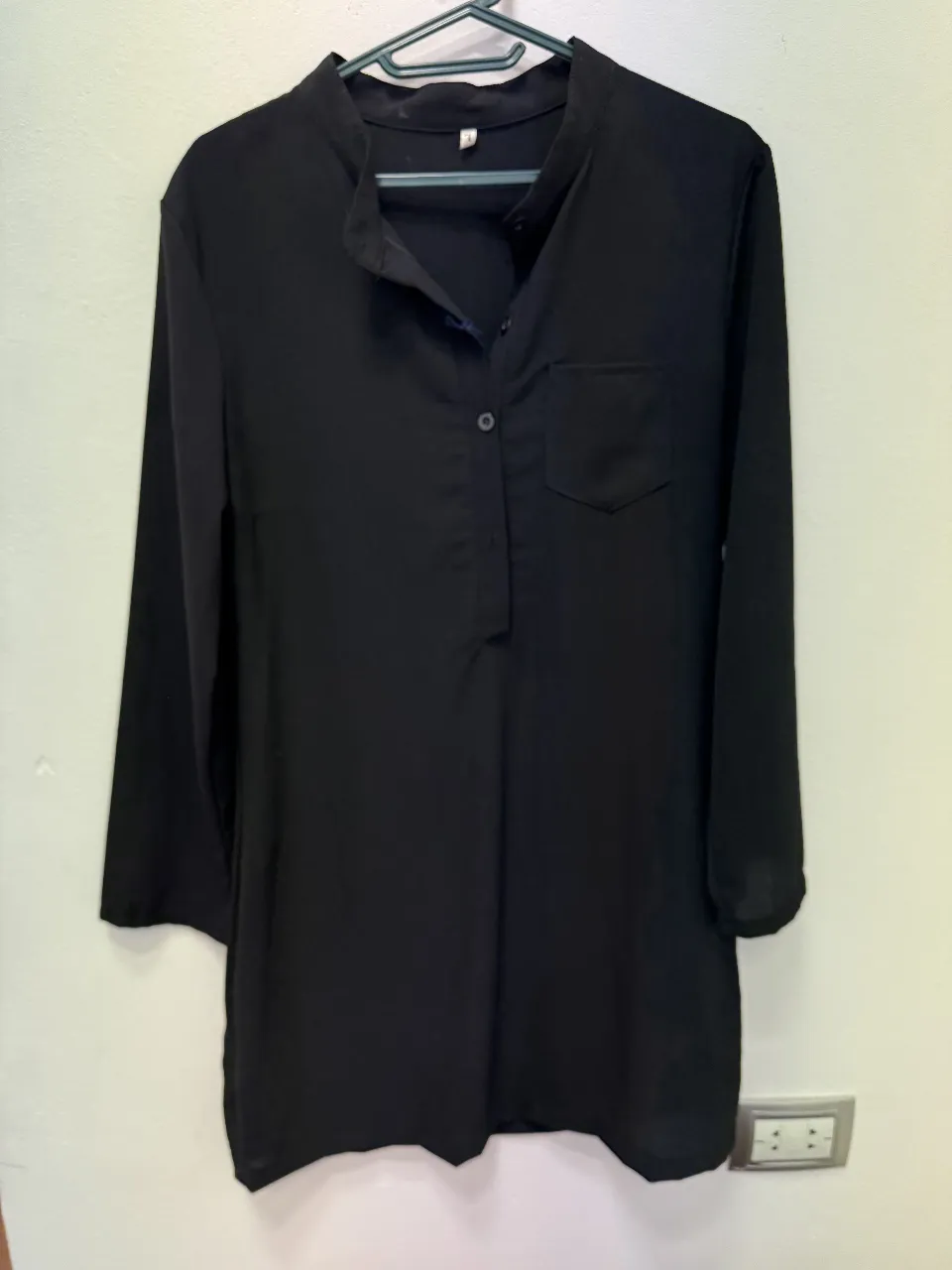 Blusa negra de manga larga con cuello mao y bolsillo en el pecho. Ideal para un look elegante y versátil.