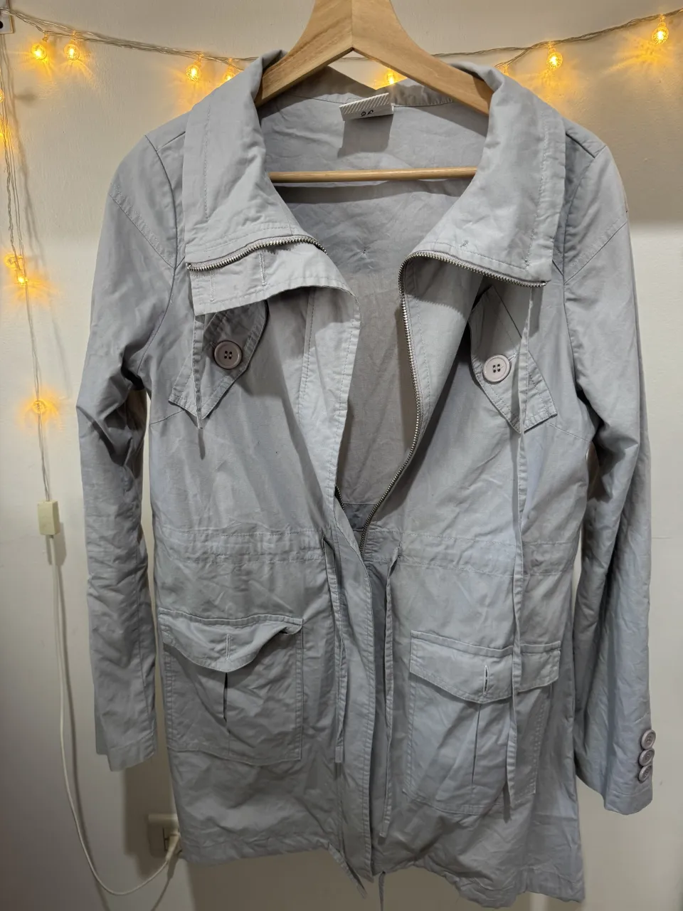 Campera gris con cuello mao, cierre al frente y cordón ajustable en la cintura. Posee dos bolsillos con solapa en la parte inferior y botones en los puños.