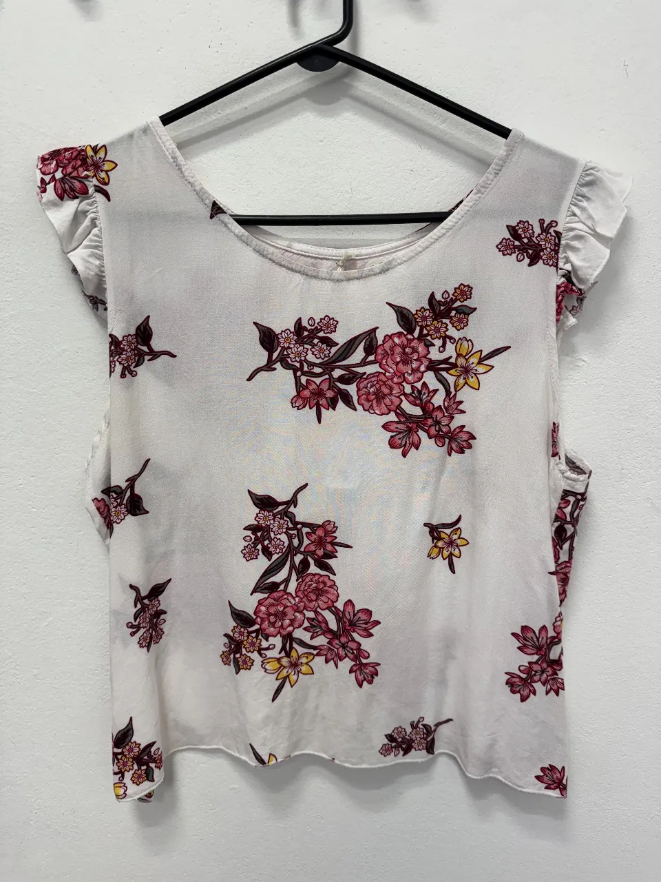 Blusa de mujer con estampado floral en tonos rosa y amarillo sobre fondo blanco. Diseño con mangas cortas con volados y escote redondo. Ideal para un look fresco y femenino.