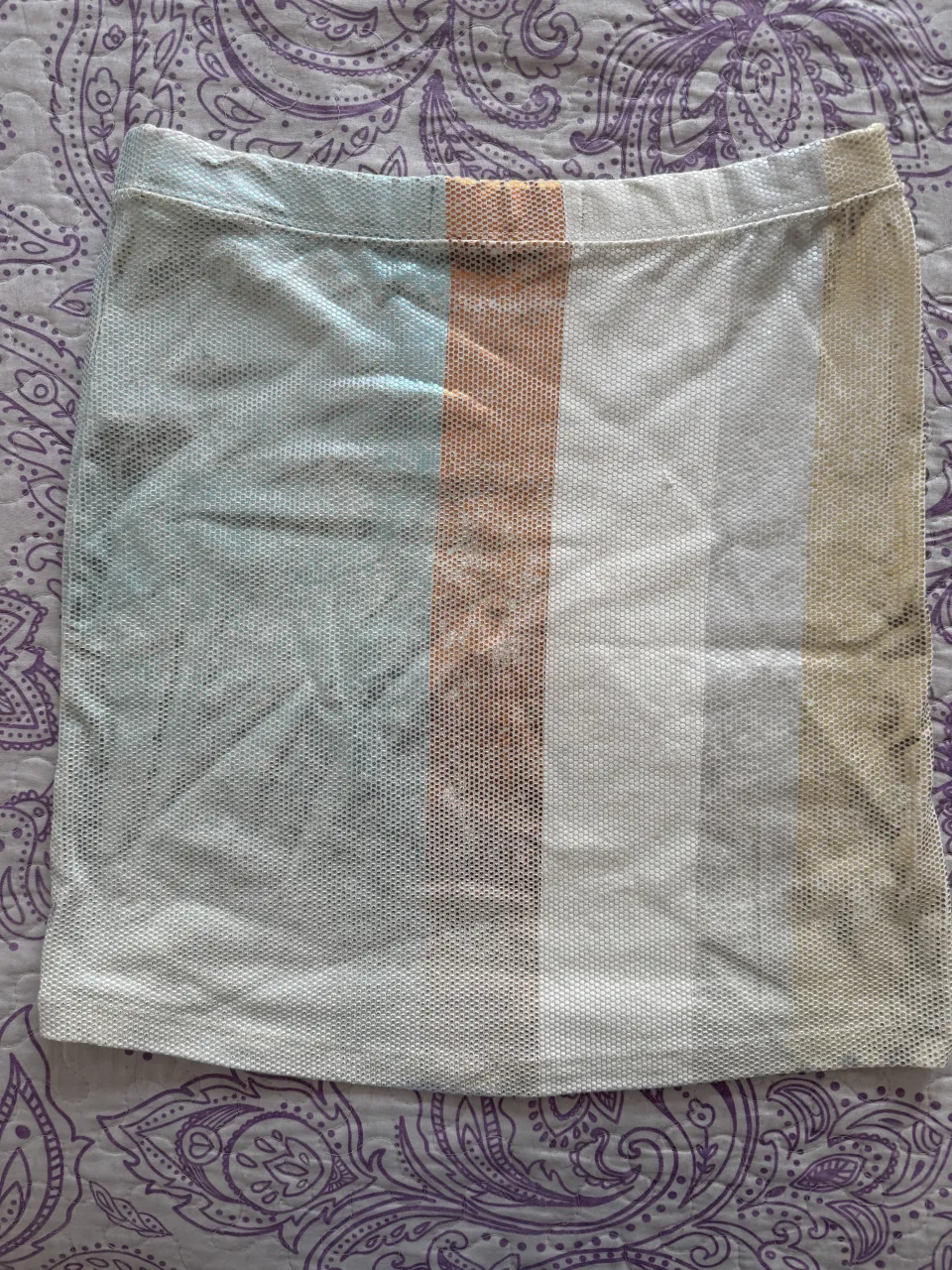 Pollera corta a rayas verticales en tonos blanco, naranja, celeste y beige. Posee un tejido calado.