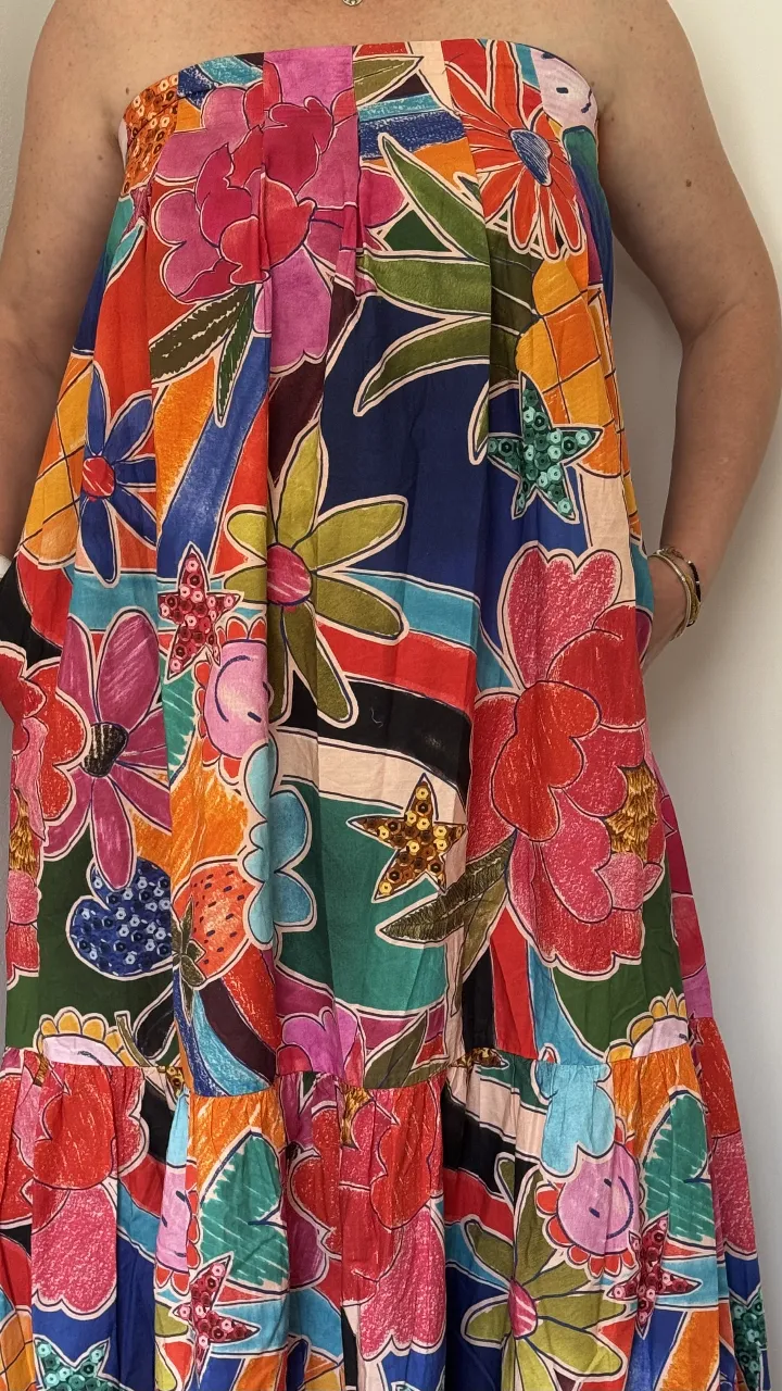 Vestido strapless largo, con estampado floral vibrante y colorido. Posee un corte amplio y volado en la parte inferior, ideal para un look veraniego y descontracturado. Cuenta con bolsillos laterales.