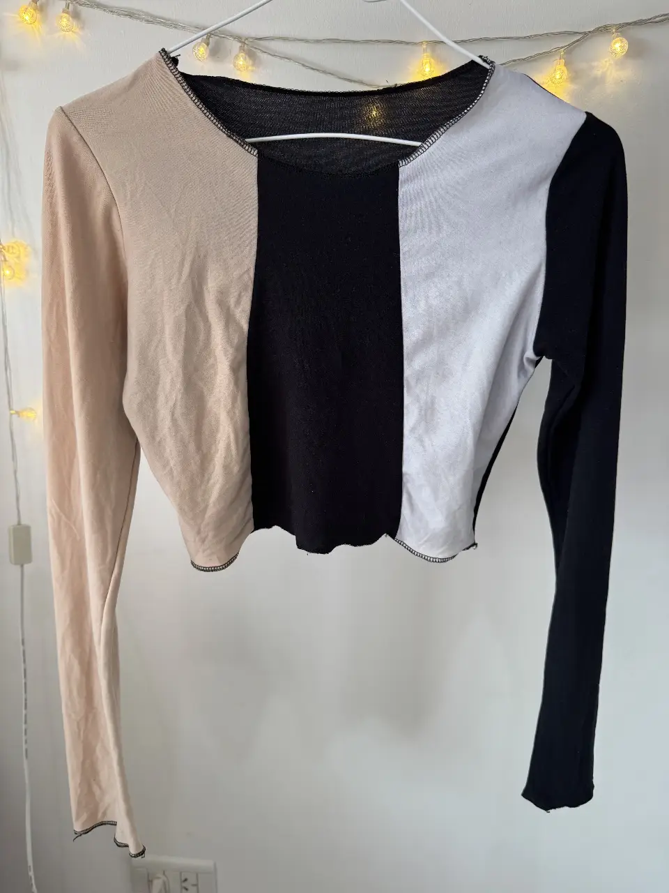 Top crop de manga larga con diseño color block en beige, negro y blanco. Ideal para un look moderno y versátil.