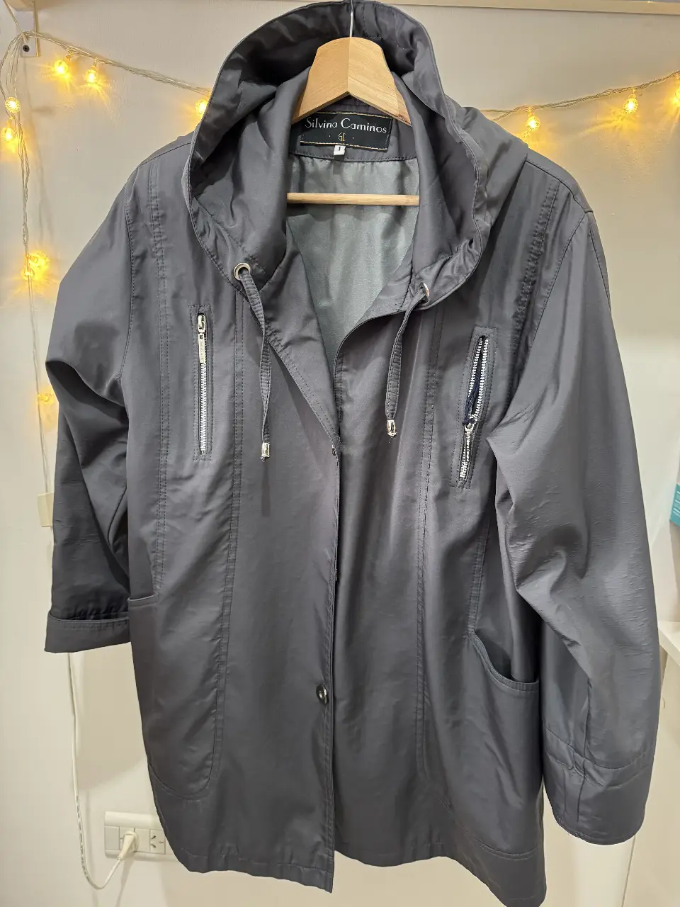 Campera gris con capucha y cierre. Tiene bolsillos con cierre y un talle 1. Ideal para usar en días de lluvia.