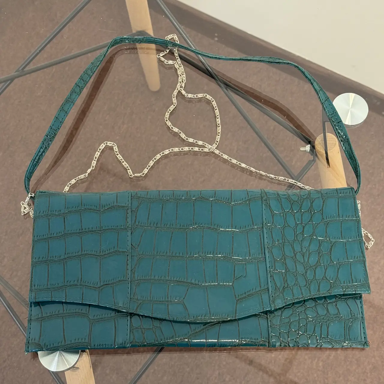 Cartera de mano de mujer, color verde oscuro con textura de reptil. Posee correa para colgar al hombro y cadena plateada. Ideal para eventos formales o salidas.