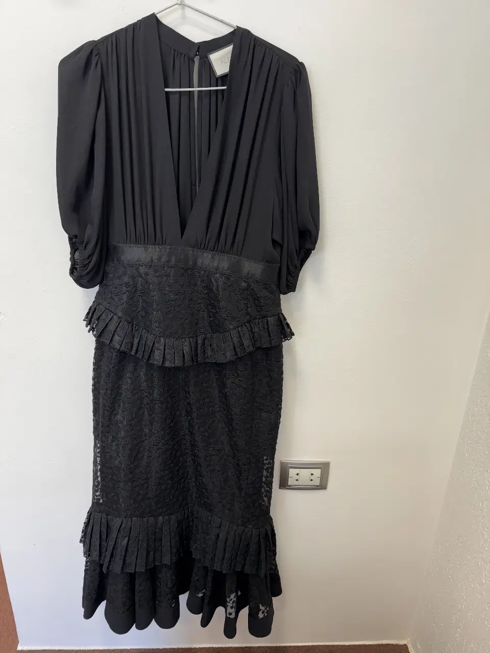 Vestido largo negro con escote en V y mangas cortas abullonadas. La cintura está adornada con una banda y volados, mientras que la falda presenta un diseño de encaje con volados en el ruedo. Ideal para eventos formales o fiestas.
