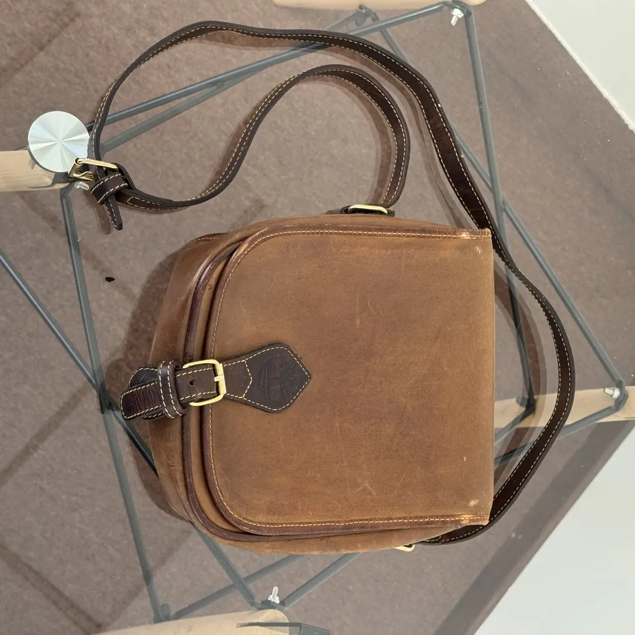 Bandolera de cuero marrón Timberland, con hebilla dorada y detalles de costura en color crema. Interior con cierre y forro naranja. Ideal para un look casual y vintage.