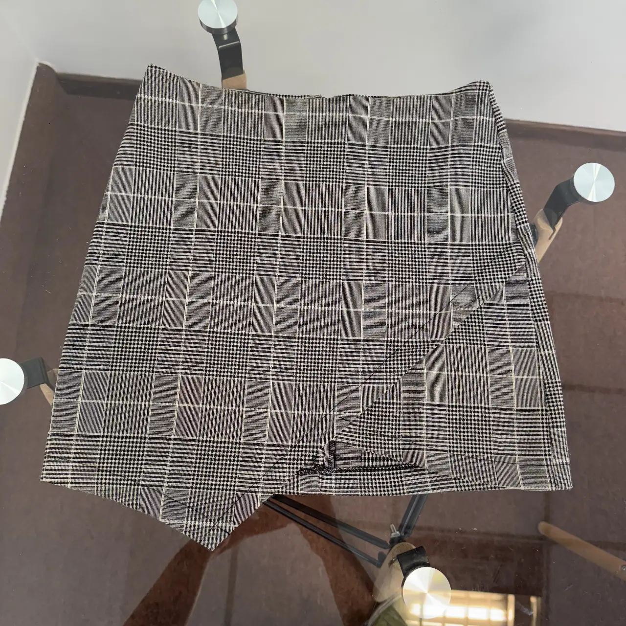 Pollera sastrera con estampado a cuadros en tonos grises y blancos. Diseño asimétrico con detalle de solapa y cierre en la parte trasera. Ideal para un look elegante y moderno.