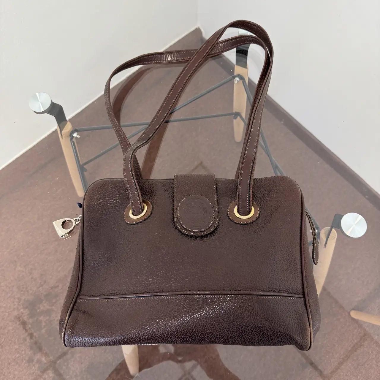 Cartera de mano vintage de cuero marrón oscuro con solapa y detalle de hebilla dorada. Interior espacioso con bolsillo interno con cierre. Ideal para un look elegante y atemporal.