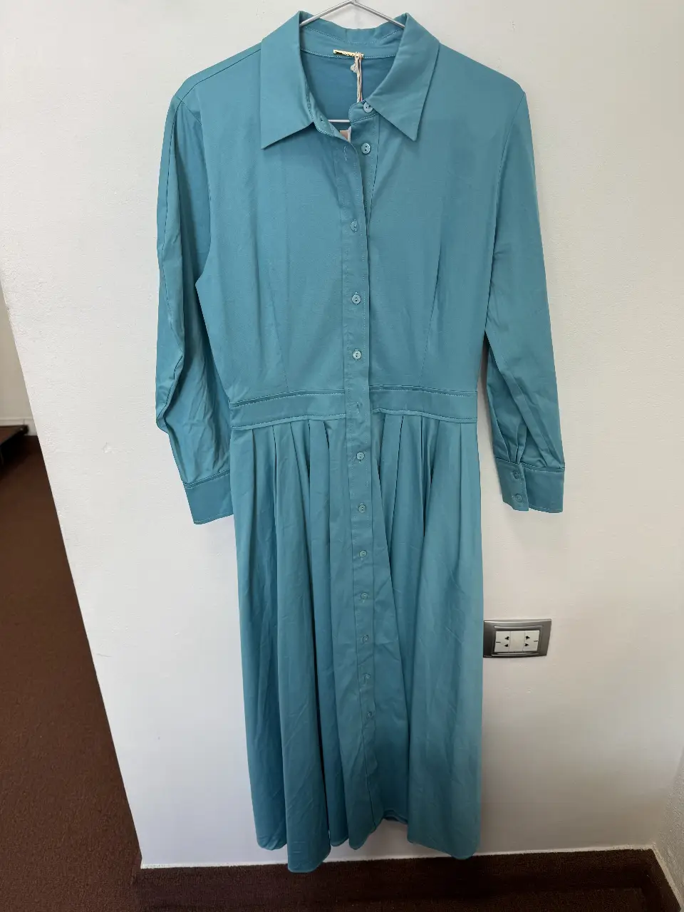 Vestido midi celeste, con cuello camisero y botones frontales. Corte en la cintura con pliegues en la falda, mangas largas con puños.