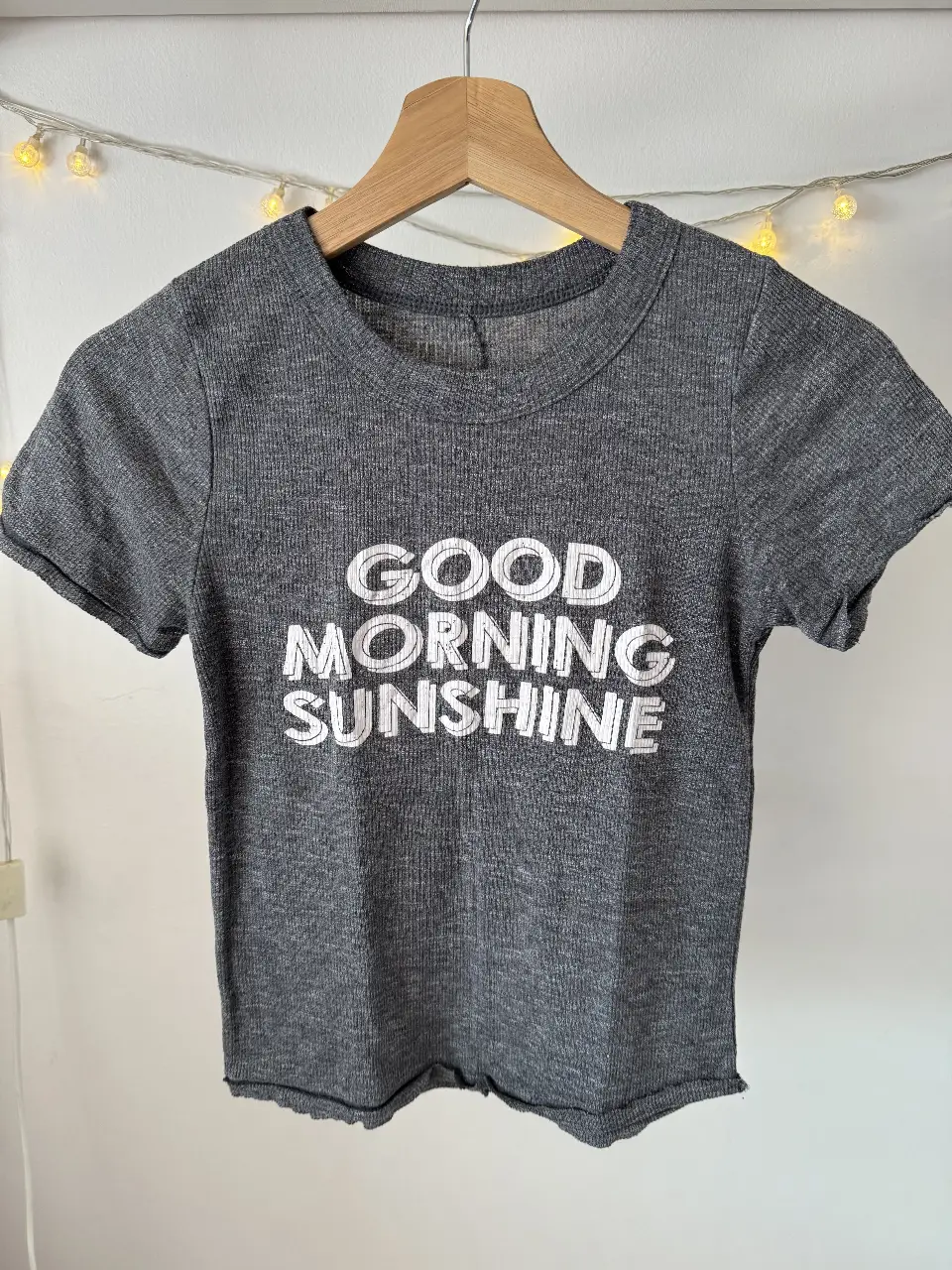 Remera de manga corta gris con estampado "GOOD MORNING SUNSHINE" en blanco. Ideal para un look casual y cómodo.
