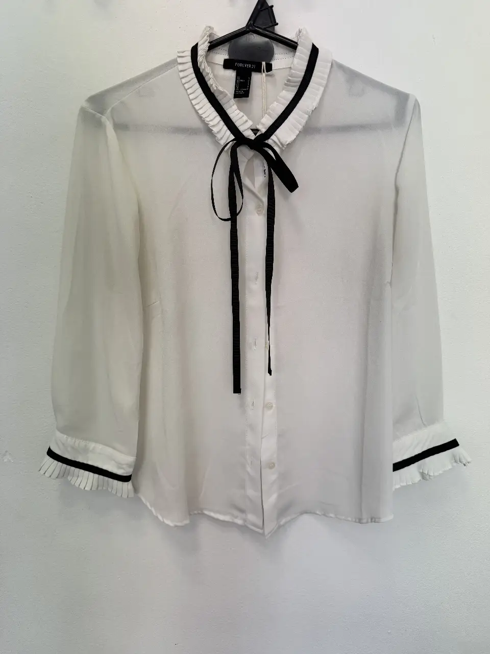 Blusa blanca de Forever 21 con detalles en negro. Cuello con volados y lazo, mangas largas con puños con volados. Ideal para un look elegante y femenino.