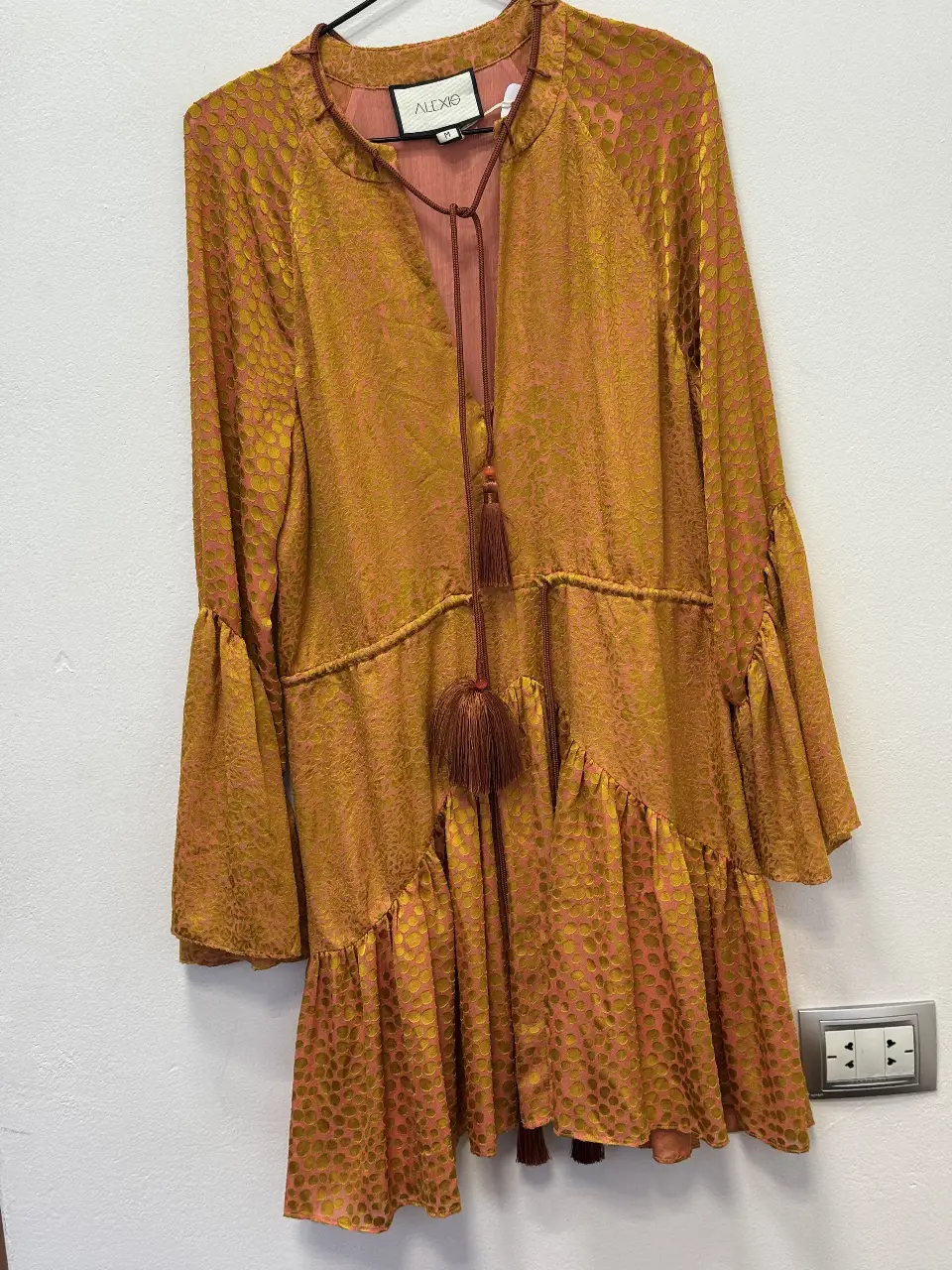 Vestido midi de la marca Alexie, con estampado de lunares en tonos dorados y rosados. Diseño con mangas largas acampanadas, detalle de lazo en el cuello y volados en la falda. Ideal para un look bohemio y elegante.