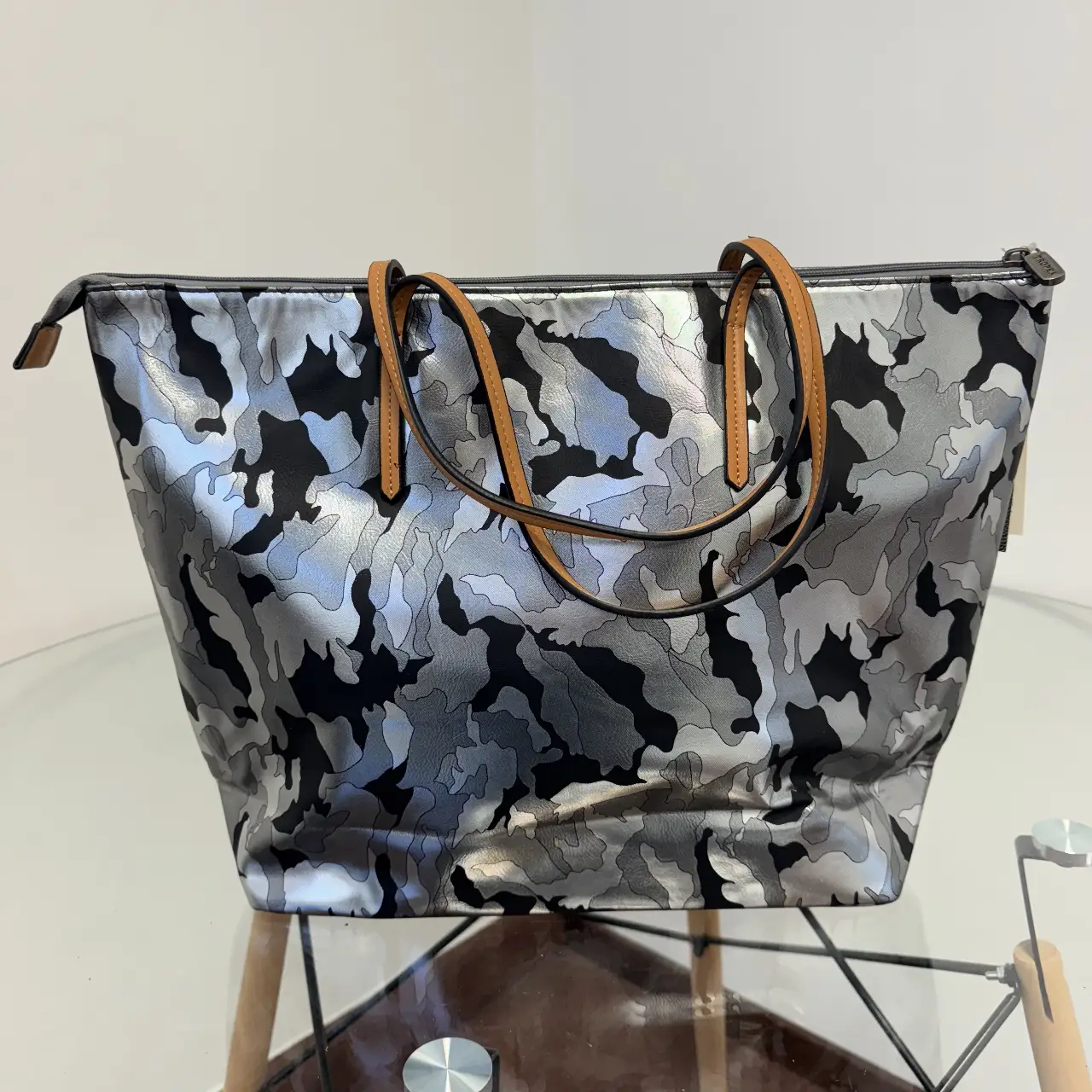 Bolso tote con estampado de camuflaje en tonos grises y negros, con detalles en marrón. Ideal para llevar todo lo necesario con estilo.