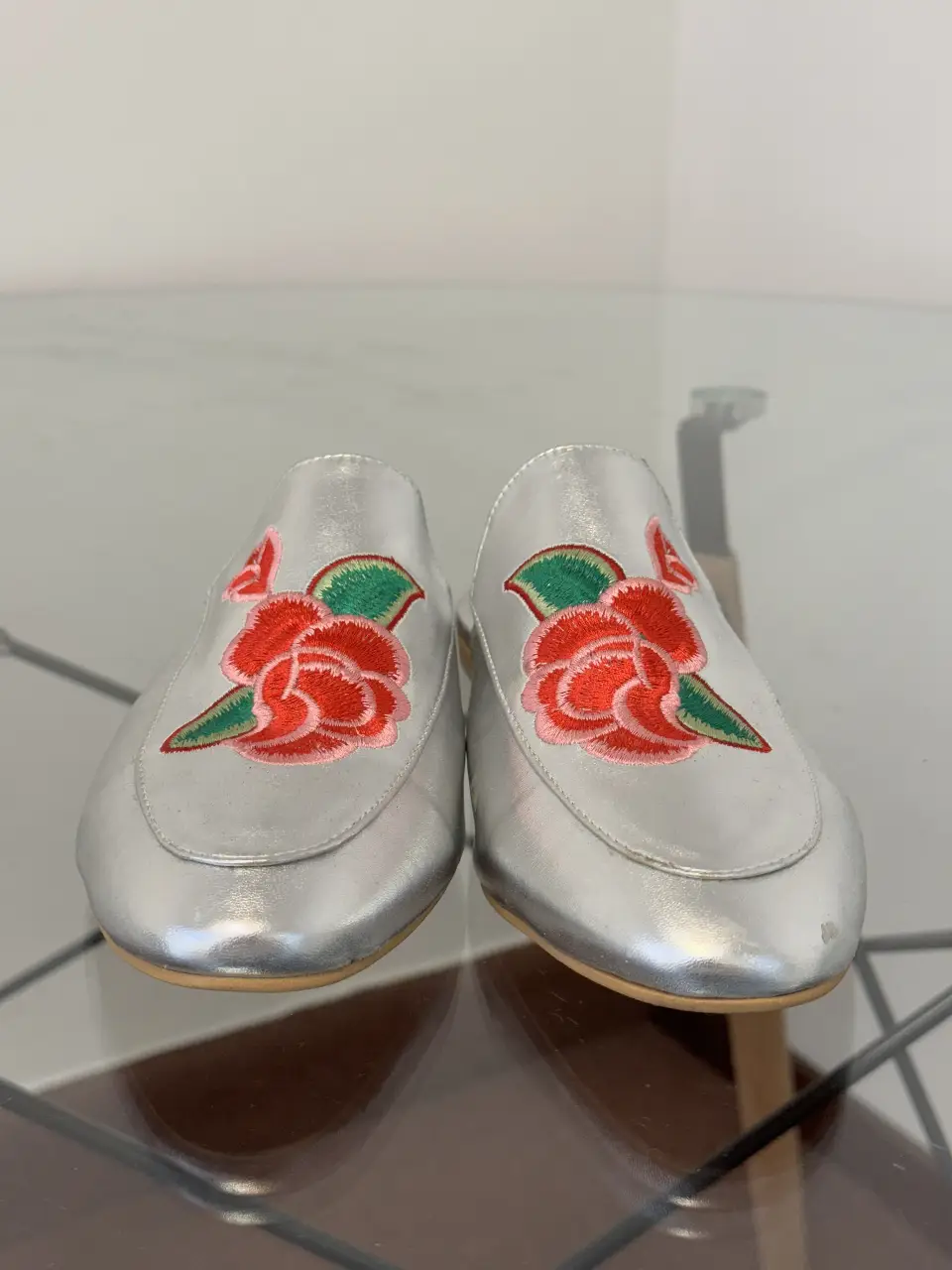 Elegantes mules plateadas con bordado floral en tonos rojos y verdes. Perfectas para un look sofisticado y femenino.
