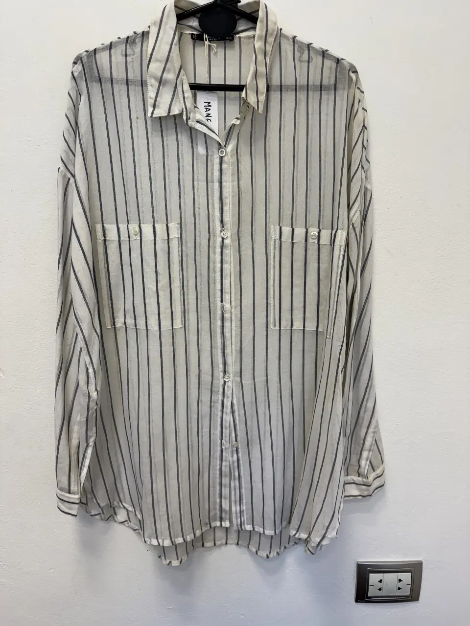 Camisa a rayas verticales en blanco y negro, con dos bolsillos delanteros y mangas largas. Ideal para un look casual y fresco.